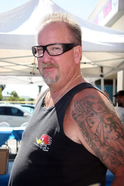 Storage Wars star Darrell Sheets wearing a brown beanie and black shirt standing in front of a white storage unit door.